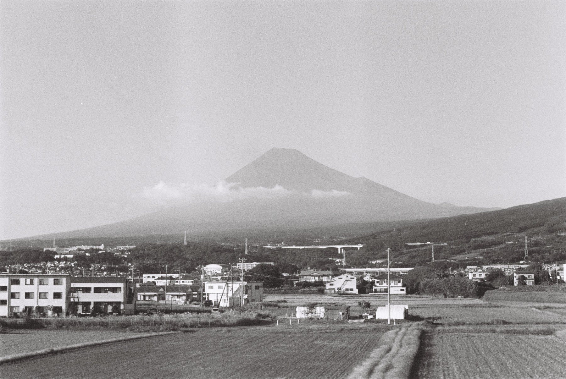 Black-and-white photograph of Mount Fuji rising above a low town and open fields.
